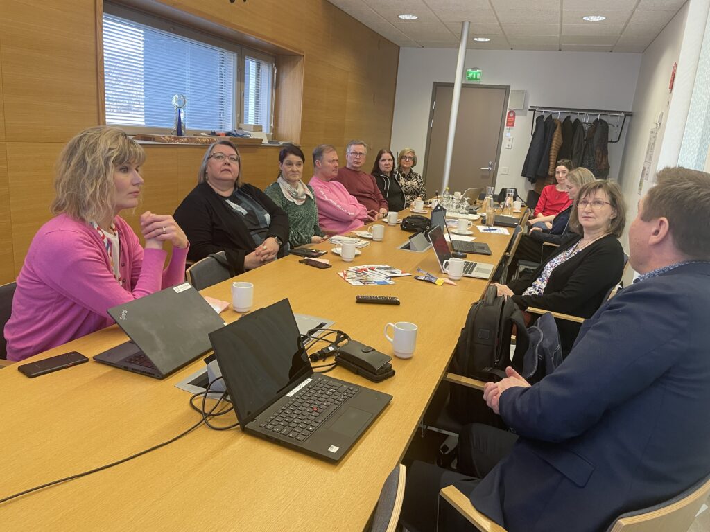 Ihmisiä kokoontuneena keskustelemaan kokoushuoneeseen pöydän ääreen.